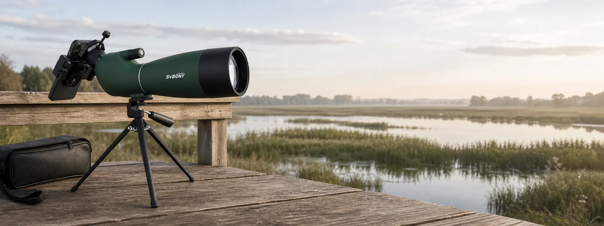Green spotting scope mounted on a tripod with smartphone adapter at a wetland viewpoint, with carry case beside it